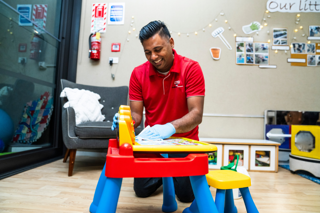 AMC commercial cleaning cleaner in red uniform providing Playschools Janitorial Cleaning in Dallas daycare center, sanitizing toys and low high surfaces