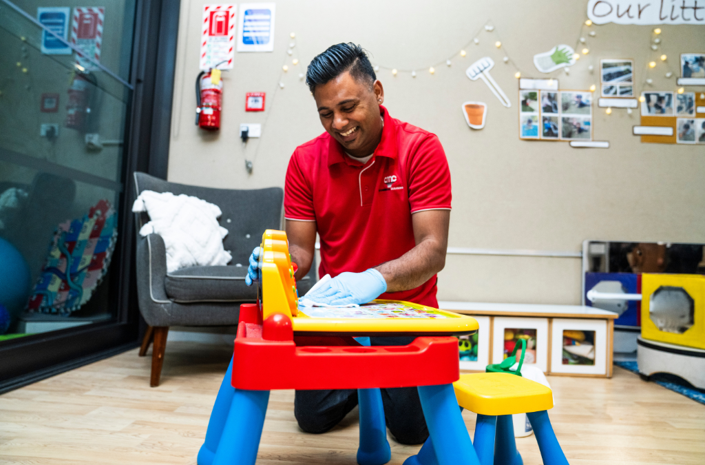 AMC commercial cleaning cleaner in red uniform providing Playschools Janitorial Cleaning in Dallas daycare center, sanitizing toys and low high surfaces