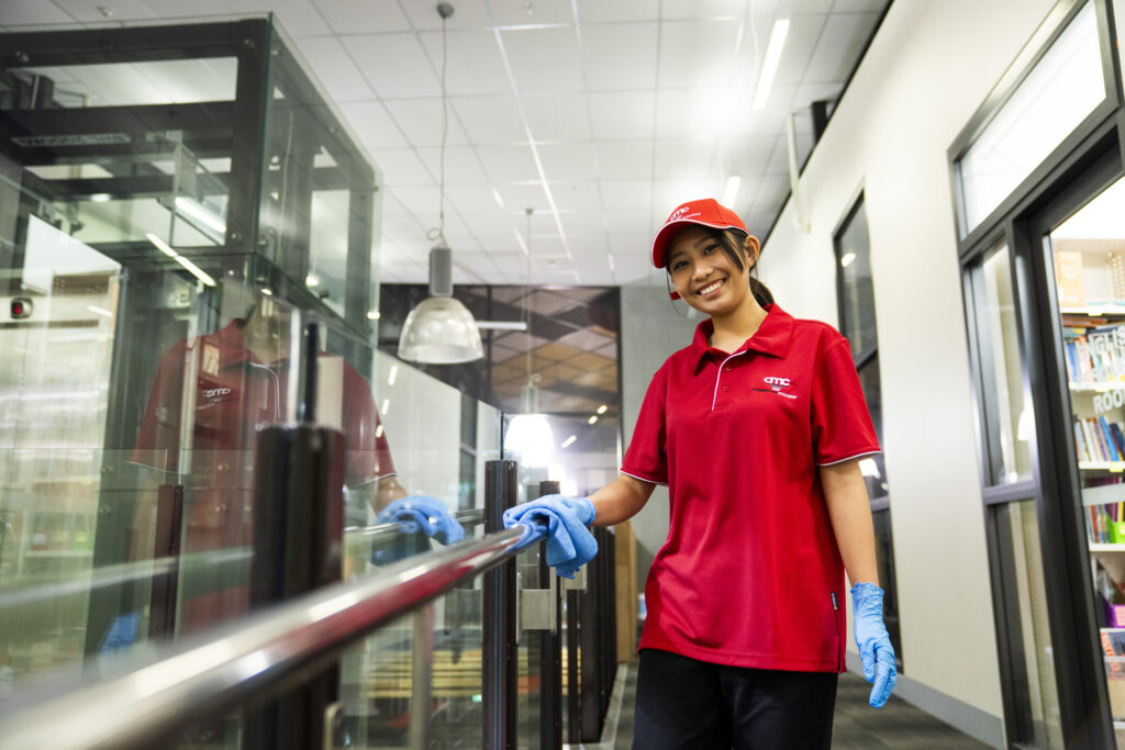 beautiful young cleaner wearing red uniform in corporate Office site in Dallas Forth Worth cleaning handle and smiling