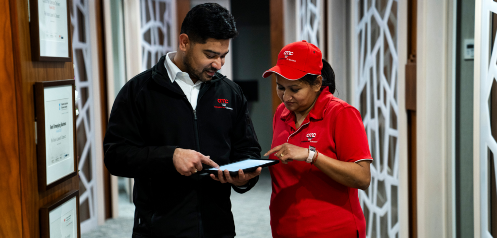 Two commercial cleaning supervisors reviewing a task checklist on a tablet in an enterprise office hallway.